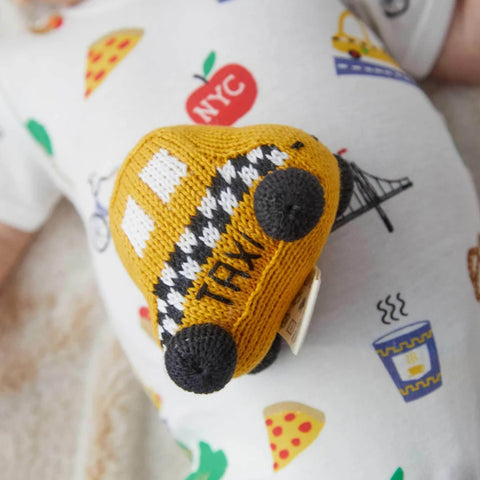 Yarn stitched rattle in the shaped of a yellow taxi with white and black accents placed on top of a baby's stomach