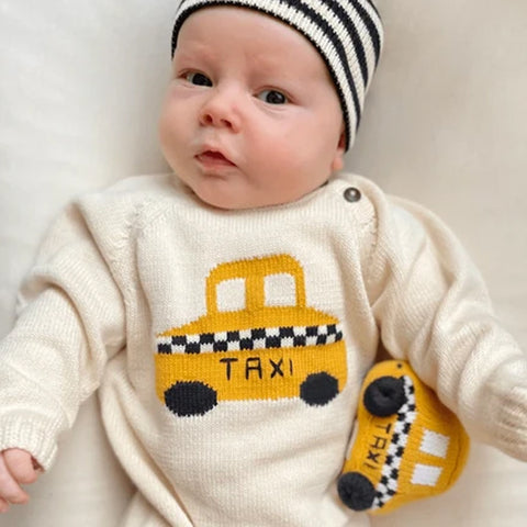 Baby with a yarn stitched rattle in the shaped of a yellow taxi with white and black accents