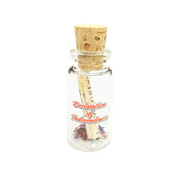 A miniature glass bottle with a beige cork with a roll of the declaration of independence with small scattering of confetti stars. The text 