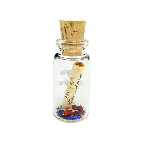A miniature glass bottle with a beige cork with a roll of the declaration of independence with small scattering of confetti stars. The text 