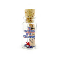 A miniature glass bottle with a beige cork with a roll of the constitution with small scattering of confetti stars. The text 
