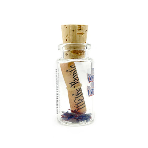 A miniature glass bottle with a beige cork with a roll of the constitution with a small scattering of confetti stars. The text 