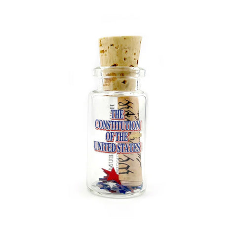 A miniature glass bottle with a beige cork with a roll of the constitution with small scattering of confetti stars. The text 