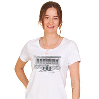 Woman wearing a white scoop neck t-shirt with the design of The New York Historical Building Facade with the text under the design 