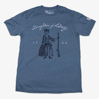 Light blue t-shirt with the illustration of a woman in a time period outfit holding a horn in one hand and a rifle in the other with the text 