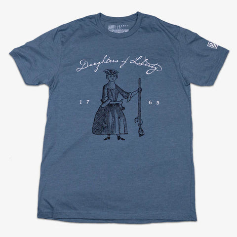 Light blue t-shirt with the illustration of a woman in a time period outfit holding a horn in one hand and a rifle in the other with the text 