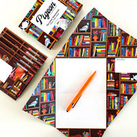 A cropped image of an array of materials spread as a top-down view. The packaging box of the letters and envelopes of the same design is placed towards the top while the letter and a pencil is placed below the frame