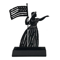 A black wooden sculpture of a silhouette of a woman in a dress with a wreath on her head holding an American flag 