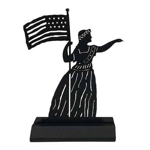 A black wooden sculpture of a silhouette of a woman in a dress with a wreath on her head holding an American flag 