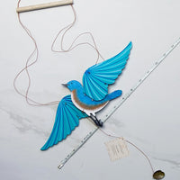 a wooden eastern bluebird mobile layed on a marble background with a ruler next to it for size reference