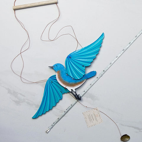 a wooden eastern bluebird mobile layed on a marble background with a ruler next to it for size reference