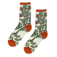 A pair of crew socks with a detailed botanical and landscape pattern on an off-white background, featuring rust orange toes, heels, and cuffs.