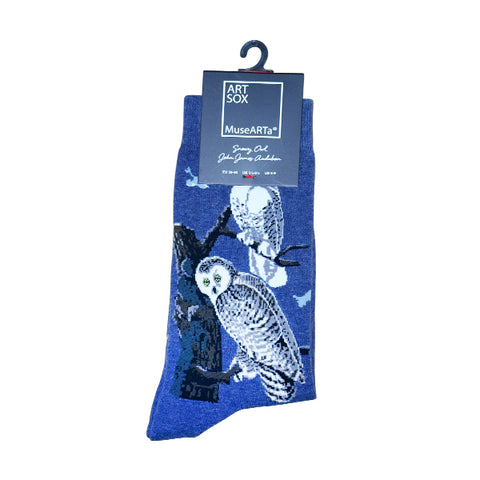 A pair of blue socks with a printed design of two owls perched on tree branches against a night sky, hanging from a black hanger with an Art Sox MuseArts tag.