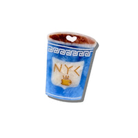 A small decorative cup-shaped brooch pin with a blue marbled body, white Greek key band, gold 'NYC' lettering, a coffee cup icon, and a brown rim with a white heart cutout