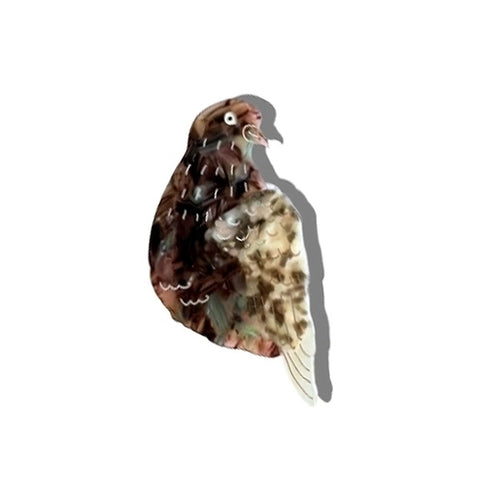 A die-cut brooch pin in the shape of a brown and beige speckled pigeon