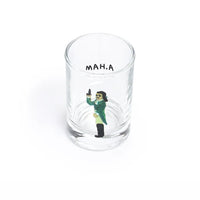 A clear shot glass featuring a printed illustration of a man in a green suit holding a gun, with the text 'A. HAM' printed on the opposite side near the rim.
