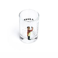 A clear glass shot glass featuring a miniature painted figure of a man holding a gun, with the word 'A. BURR' printed on the opposite side in black near the rim.