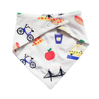 A back view of a white triangular bandana bib featuring a colorful New York City-themed print with illustrations of a bicycle, hot dog, pizza, coffee cup, bridge, taxi, and red NYC logos.