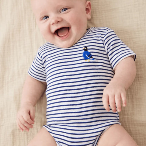 A baby wearing a blue pinstripe bodysuit with small emblem on the right chest of a blue and black pigeon with yellow accents
