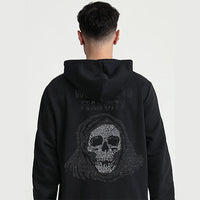 A man viewed from behind, wearing a black hoodie with a large hooded skull graphic on the back made of small rhinestones, against a plain light gray background.