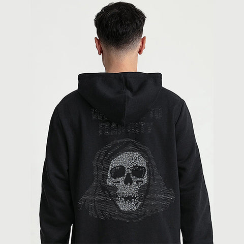 A man viewed from behind, wearing a black hoodie with a large hooded skull graphic on the back made of small rhinestones, against a plain light gray background.