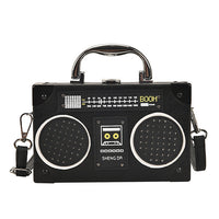 A black retro-style boombox handbag with a top handle and shoulder strap, featuring speaker grilles, a faux dial control panel, and the brand name 'SHENG DA' on the front, shown against a plain white background.
