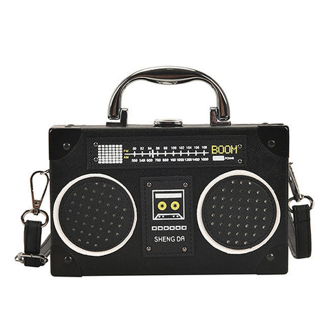 A black retro-style boombox handbag with a top handle and shoulder strap, featuring speaker grilles, a faux dial control panel, and the brand name 'SHENG DA' on the front, shown against a plain white background.