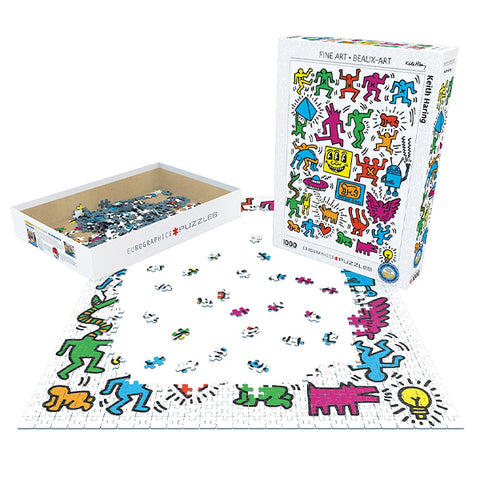 A colorful puzzle set is shown with its illustrated box, an open box of puzzle pieces, and a partially assembled puzzle on a white background. The artwork features playful cartoon figures in bright, multicolored tones by Keith Haring.