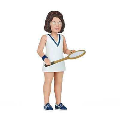 A side view of a woman with brown hair wearing eyeglasses and a white tennis dress with a blue v accent collar holding a tennis racket with blue tennis sneakers and light blue laces 